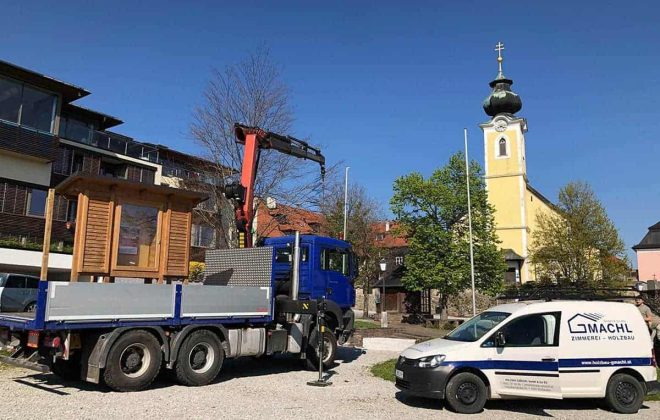 Lkw und Gmachl-Handwerkerauto transportieren Holzbau in Salzburg, Kirche im Hintergrund