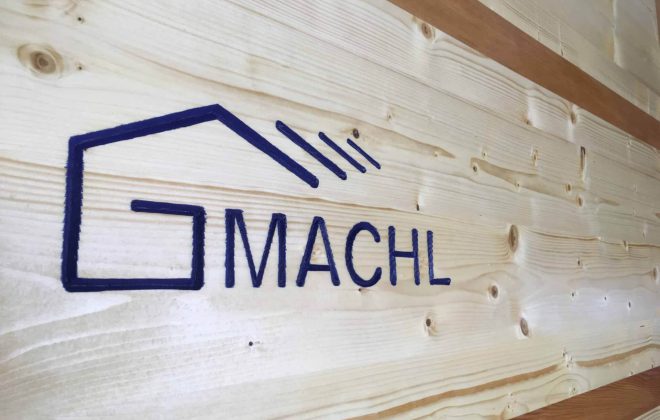 Holzbau Gmachl Logo auf hellen Holzbrettern, Zimmerei Salzburg, moderner Holzbau, Dachstuhl